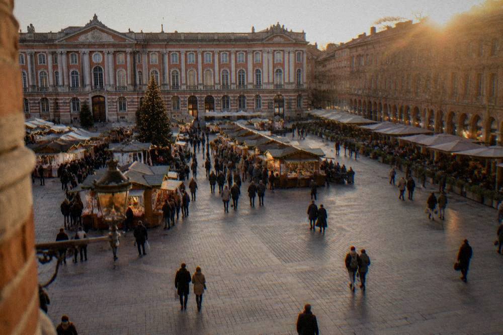 A lit Christmas market with wooden stalls in front of a grand city hall facade