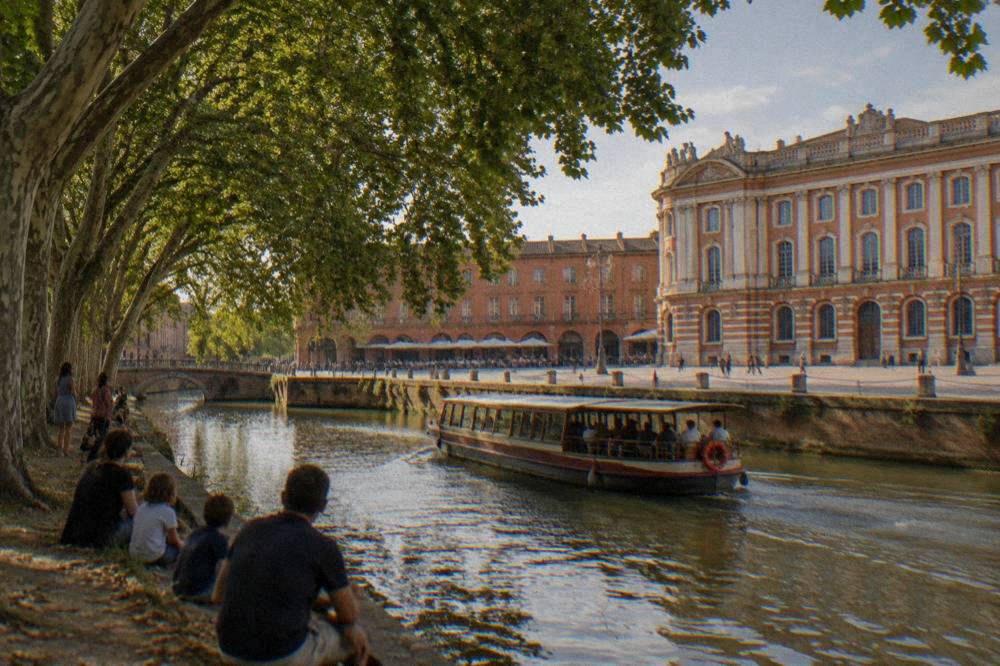 A canal boat passing under plane trees while families watch from the bank