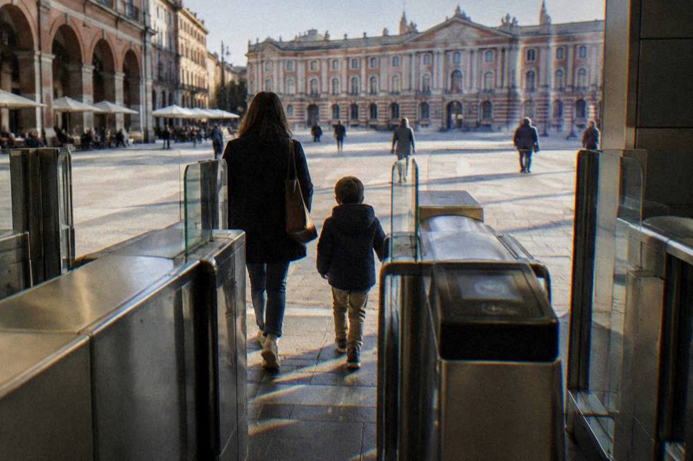 A parent and child passing through a modern metro station gate in Toulouse